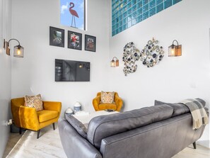 A modern living room with a sofa, two armchairs, a flat-screen TV, wall art, and decorative lighting. - Ocean Mist Cottage (Carna)