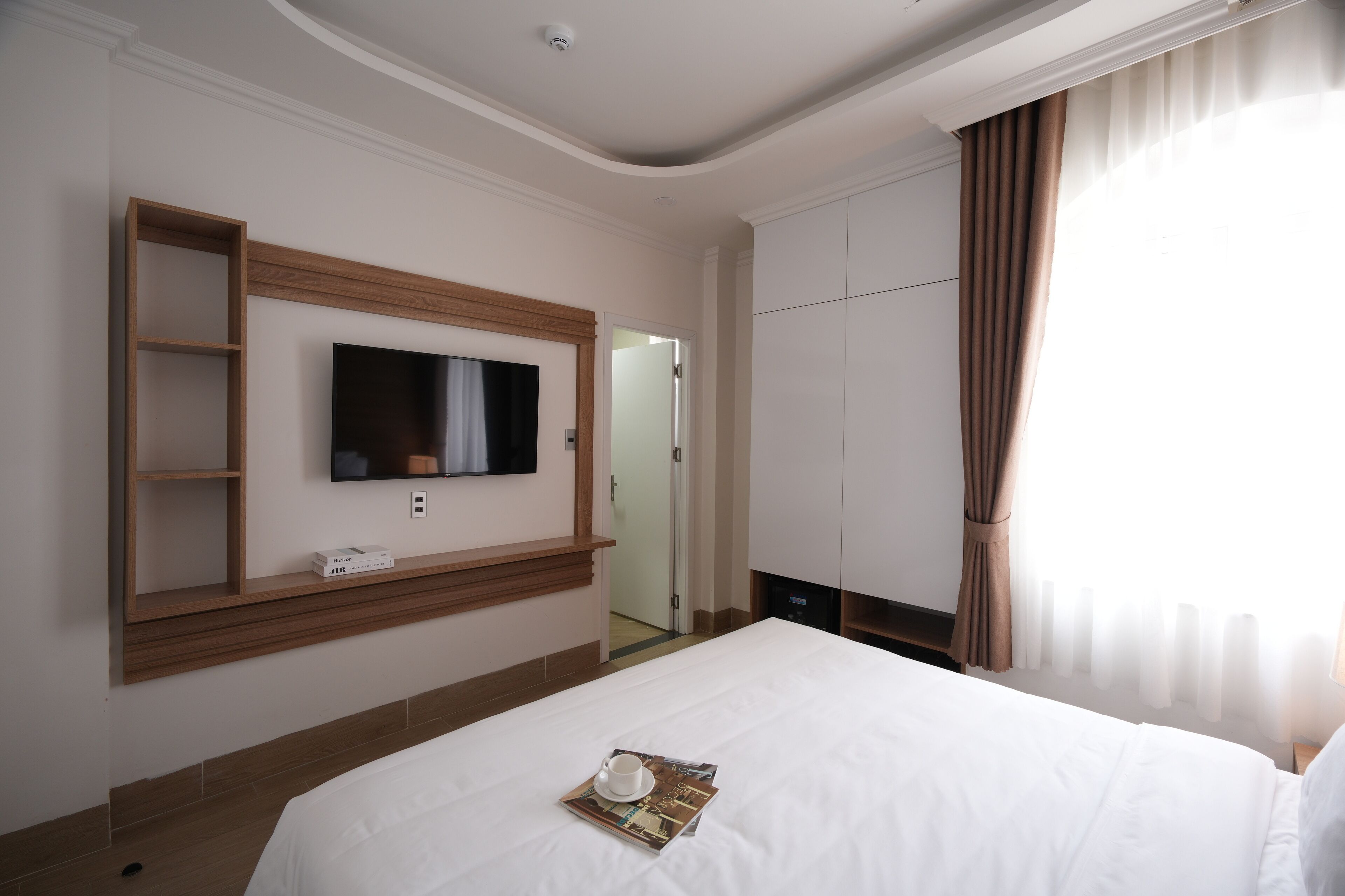 A hotel room with a large bed, a mounted TV, a wooden shelf, and a wardrobe.