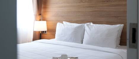 A hotel room with a wooden headboard, a bed with white linens, a bedside lamp, and a window with curtains.