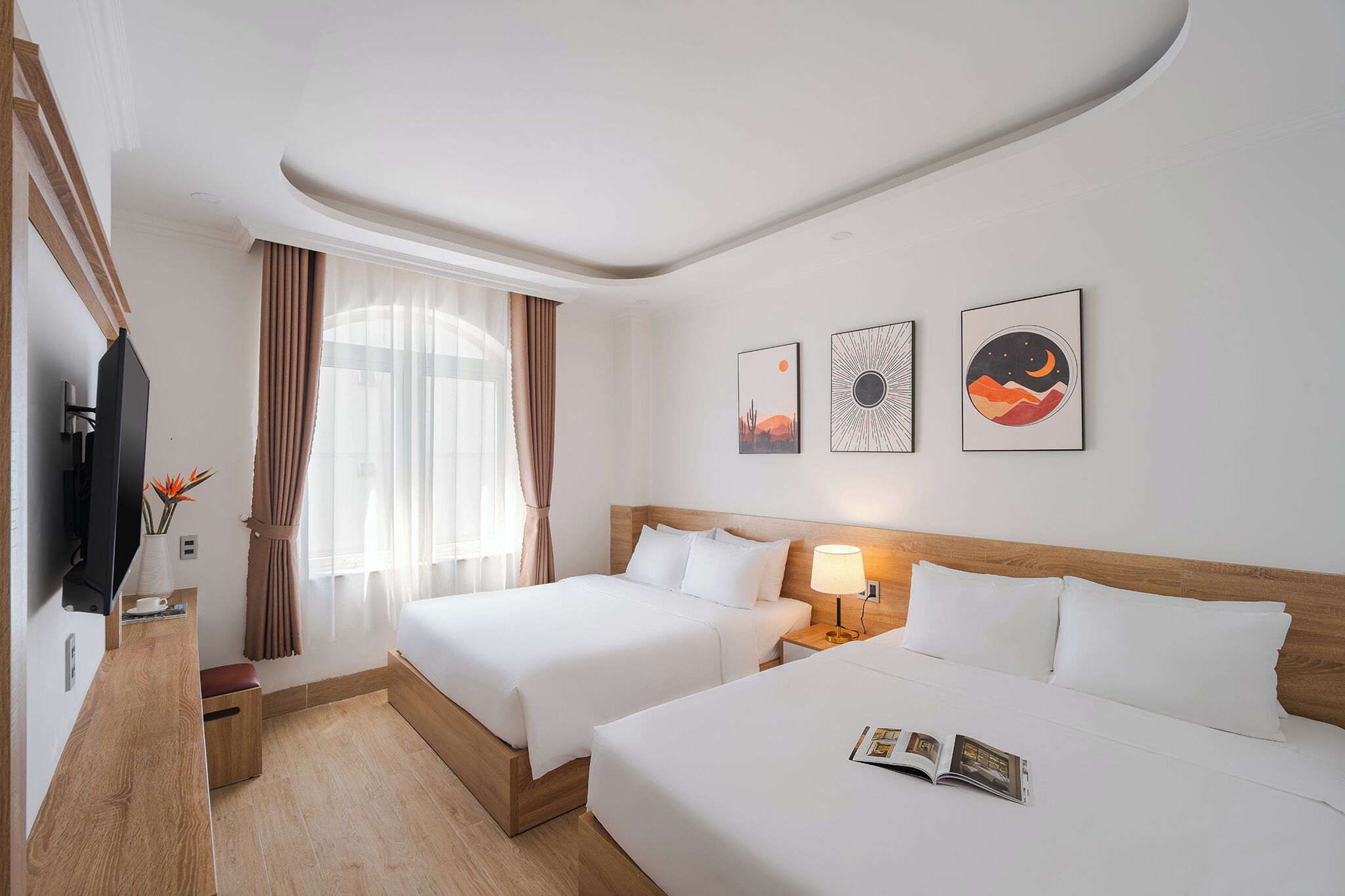 A hotel room with two beds, a TV, a bedside table with a lamp, and artwork on the wall.