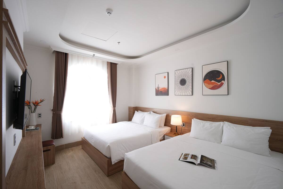 Habitación de hotel con dos camas, televisión, escritorio y ventana con cortinas.