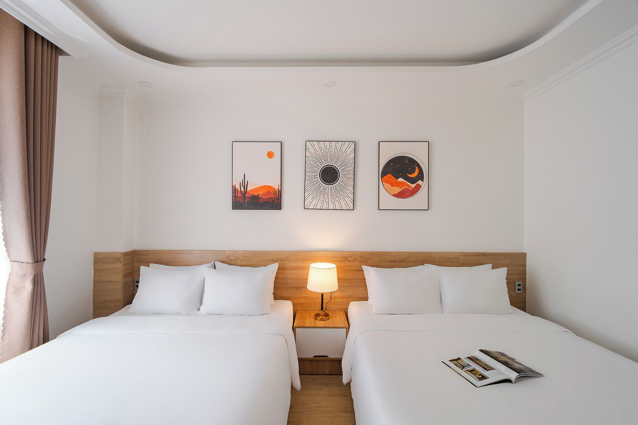Ein Hotelzimmer mit zwei Betten, einem hölzernen Kopfteil, einem Nachttisch mit Lampe und drei gerahmten Kunstwerken an der Wand.