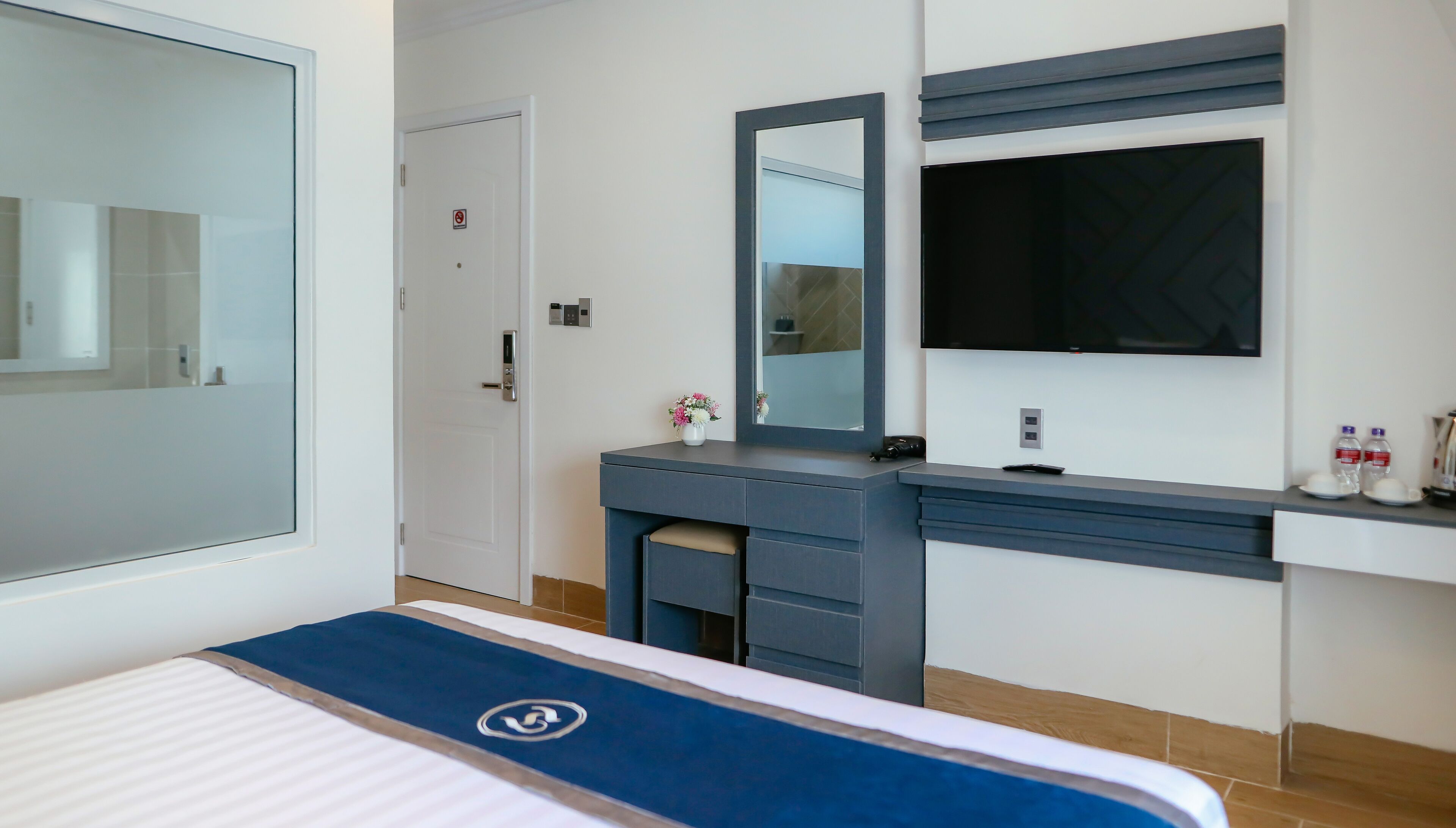 Une chambre d’hôtel moderne équipée d’un lit, d’une coiffeuse avec un miroir, d’un téléviseur à écran plat et d’une porte sur laquelle est apposée une pancarte « accès interdit ».