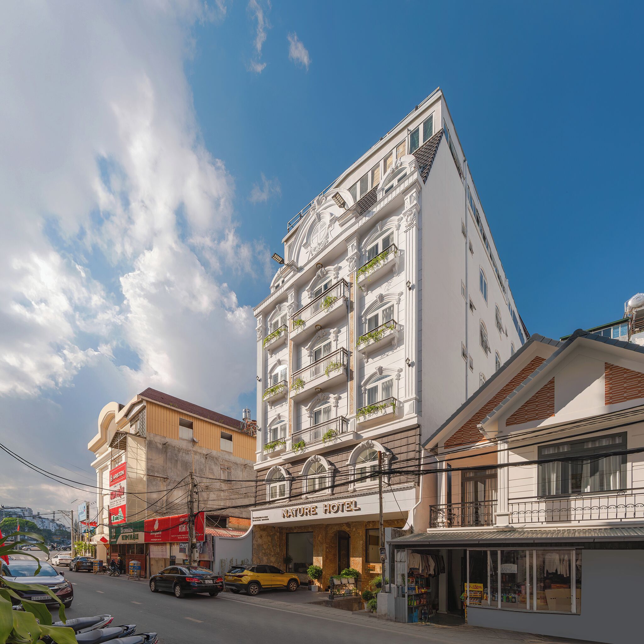 A hotel with a white facade, multiple balconies, and a sign reading 'NATURE HOTEL'.