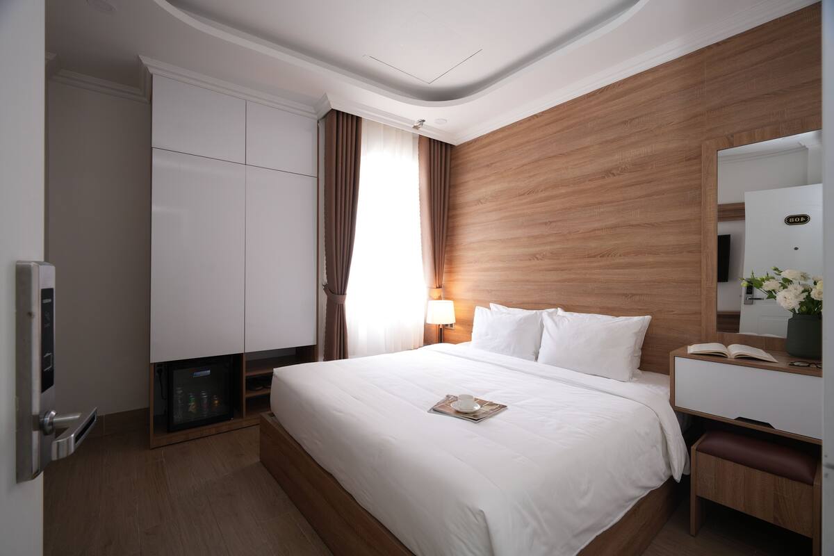 Habitación de hotel con una cama grande, cabecera de madera, armario, escritorio con espejo y mesita de noche.