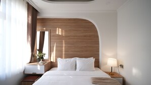 A hotel room with a large bed, a wooden headboard, a bedside table with a lamp, and a small bench. - Nature Hotel - Le Dai Hanh (Xuan Huong - Da Lat)