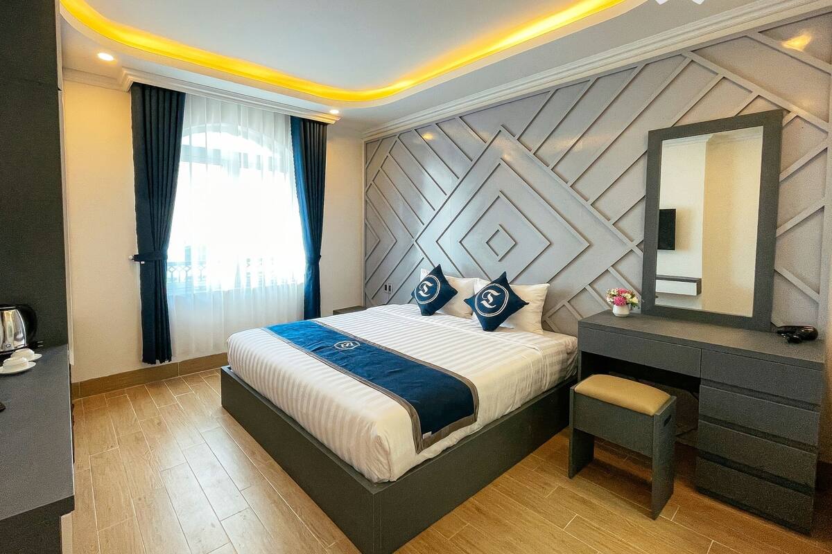 Una habitación de hotel con cama, escritorio, silla, espejo y ventana con cortinas.