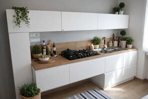 Una cucina moderna con mobili bianchi, un piano di lavoro in legno, un fornello a gas e diversi utensili da cucina e piante.