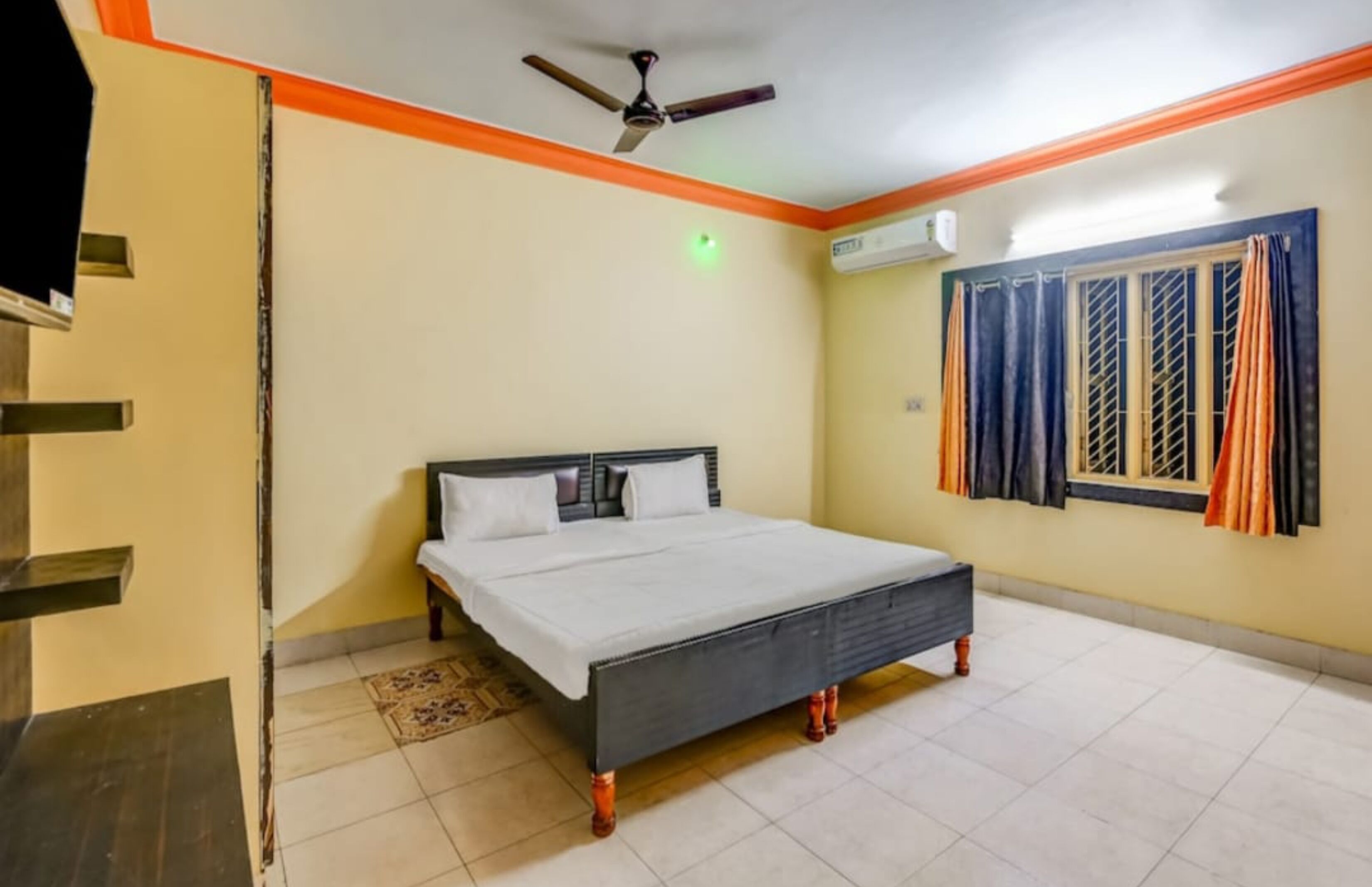 A bedroom with a bed, a ceiling fan, an air conditioning unit, and a window with curtains.