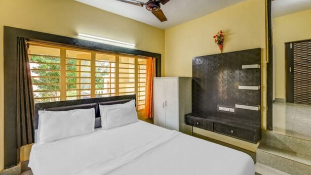 A bedroom with a bed, a wardrobe, a ceiling fan, and a window with curtains. - DhamStay Hotel Moon Near Niladri Beach (Puri)