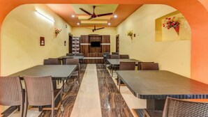 A dining area with multiple tables and chairs, a ceiling fan, and decorative wall elements. - DhamStay Hotel Moon Near Niladri Beach (Puri)