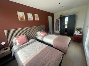 Une chambre d’hôtel avec deux lits, une armoire, une coiffeuse avec un miroir et un mur orné de trois tableaux encadrés.