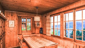 A wooden cabin with a large dining table, chairs, and a bench. There are windows with curtains, a hanging light fixture, and a clock on the wall. - Beautiful private villa for 6 guests with WIFI, TV, terrace and panoramic view (Les Collons)