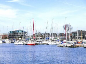 A marina with multiple boats docked, a crane, and modern buildings in the background.