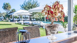 Una mesa de comedor con un florero de vidrio, sillas de mimbre y vistas a sombrillas y sillones de exterior.