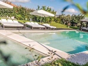 Ein Schwimmbecken mit Liegestühlen und Sonnenschirmen, umgeben von viel Grün.