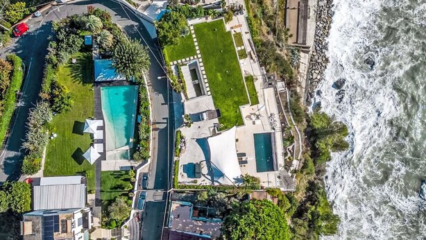 Vista aérea de una propiedad costera con varias construcciones, una piscina y acceso directo a la playa.