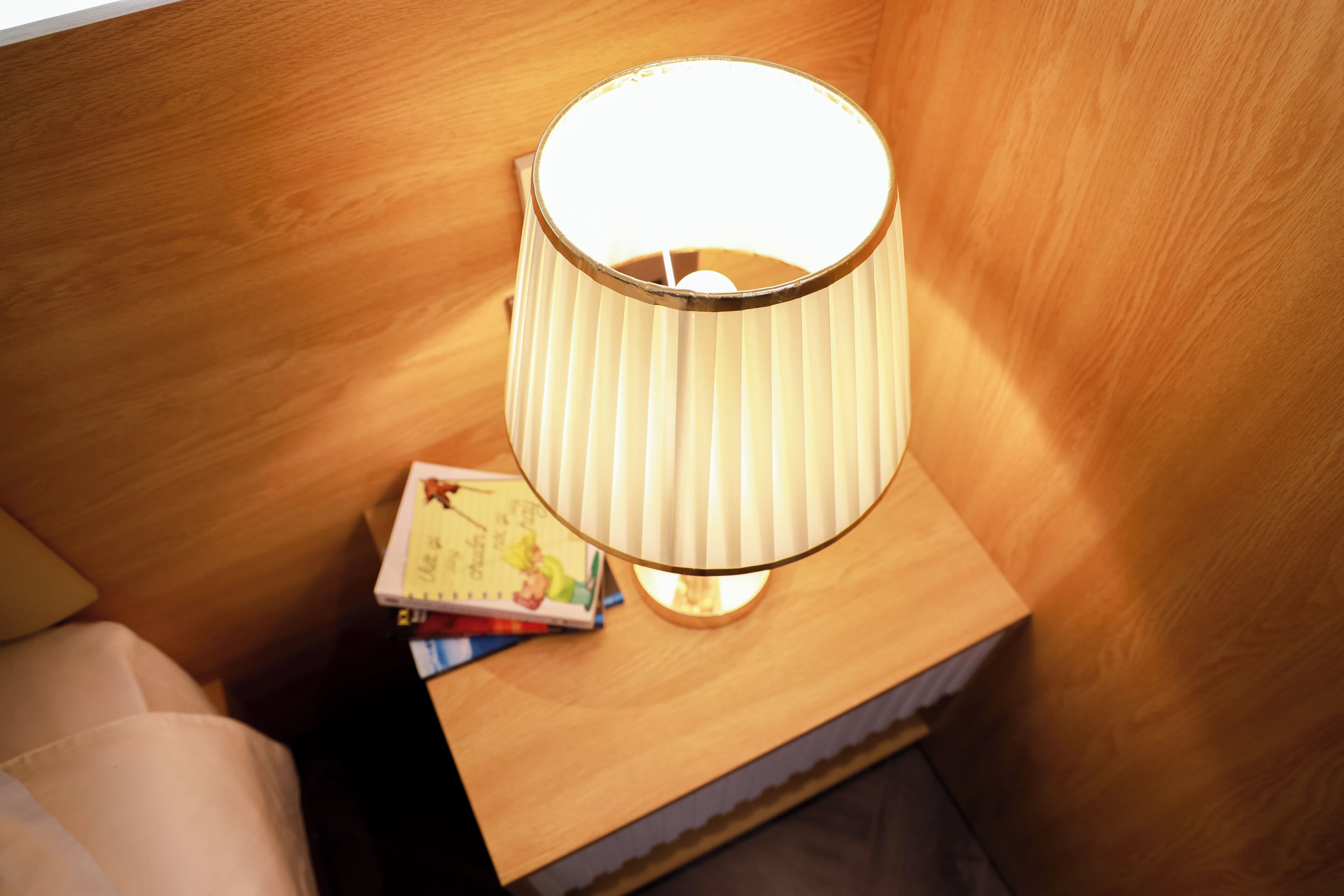 A wooden bedside table with a lamp and a book.