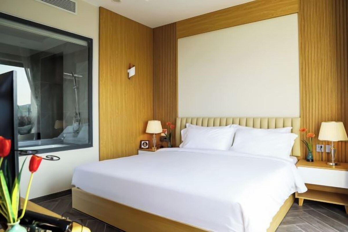 A hotel room with a large bed, wooden paneling, a television, and a nightstand with a lamp and flowers.