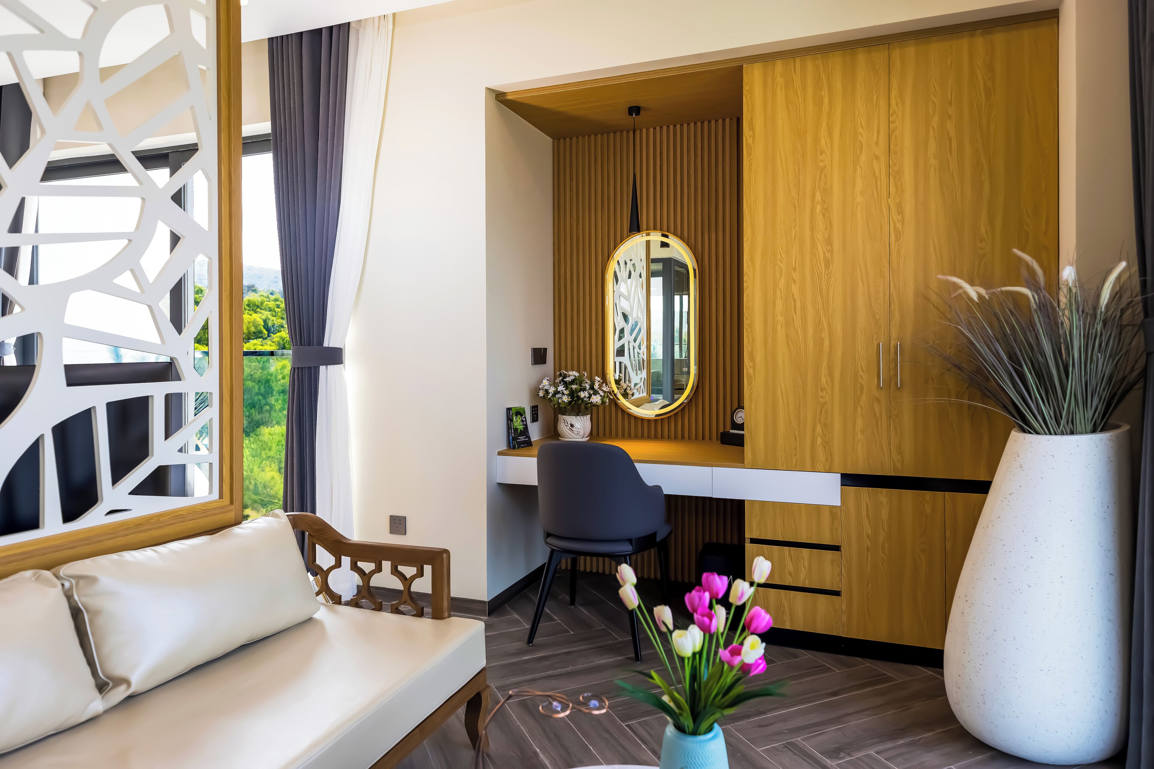 A modern room with a wooden desk, a large mirror, a sofa, and a potted plant.