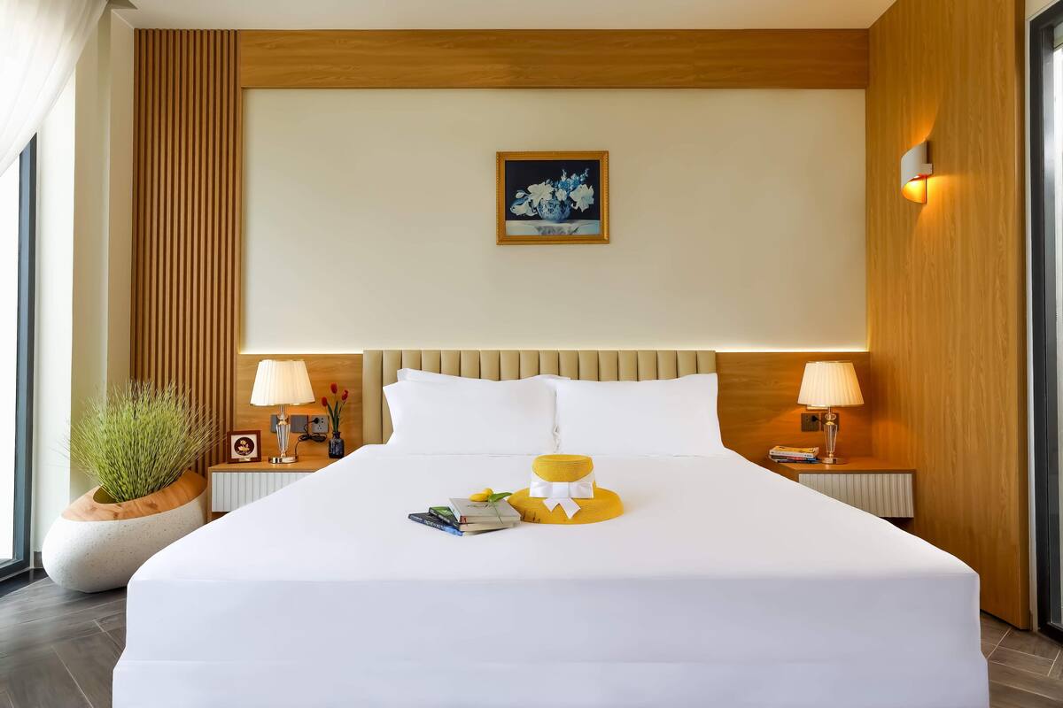 Une chambre d’hôtel avec un grand lit, deux lampes de chevet, une œuvre d’art encadrée au mur et une plante en pot près du lit.