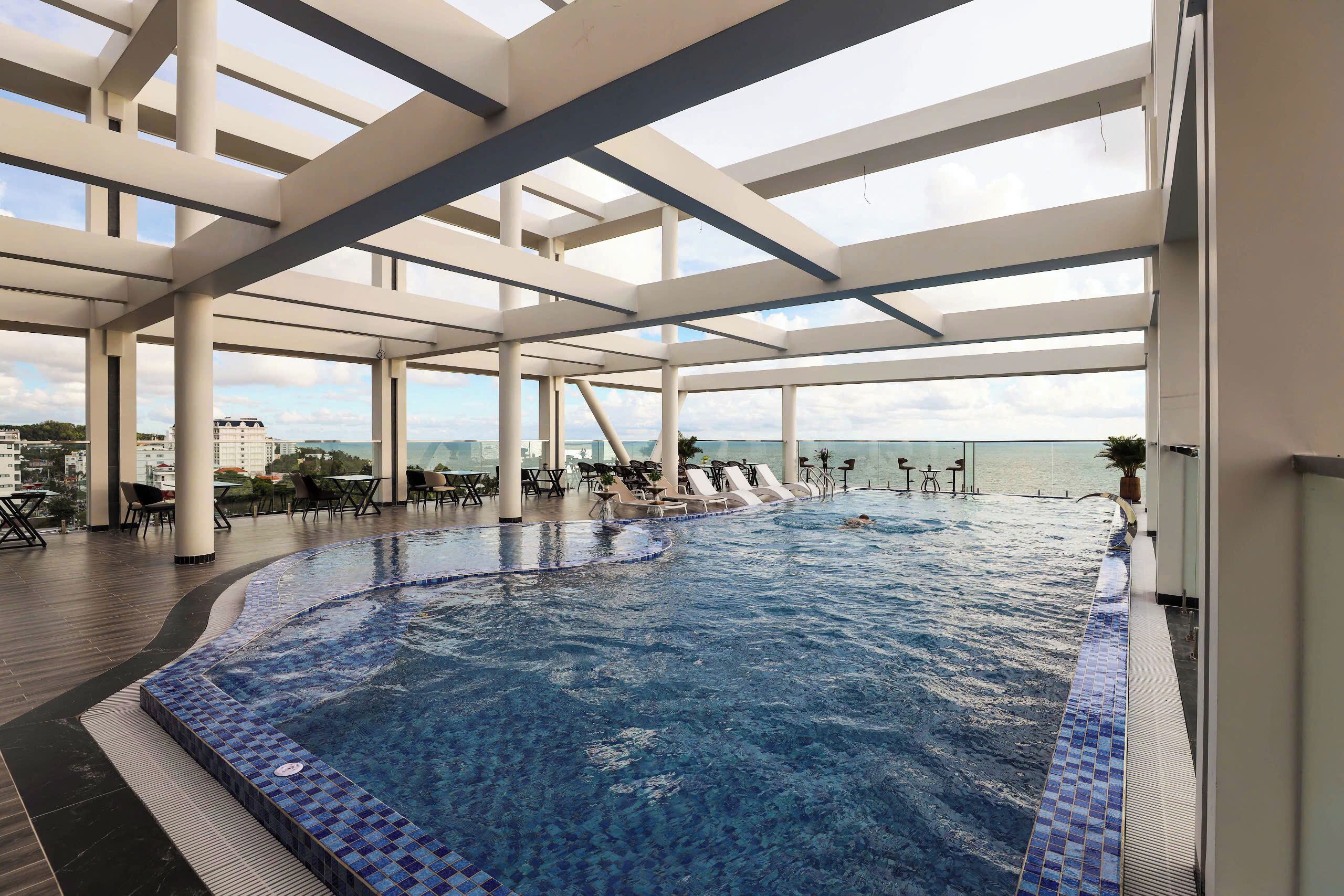 An indoor swimming pool with clear blue water, surrounded by white pillars and a view of the sea.