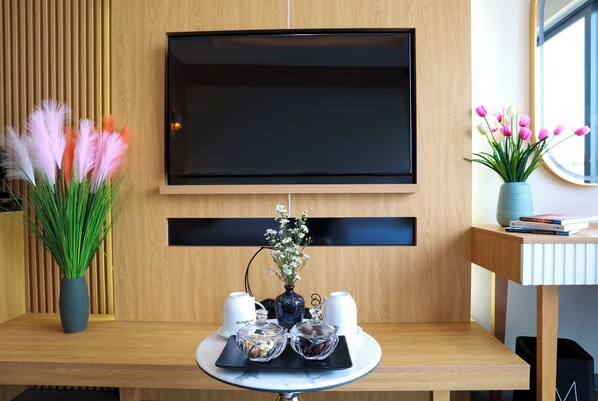 A modern living room with a flat-screen TV mounted on a wooden wall, a coffee table with decorative items, and a window with a view of tulips. - Daystar Hotel Phu Quoc (Phu Quoc)