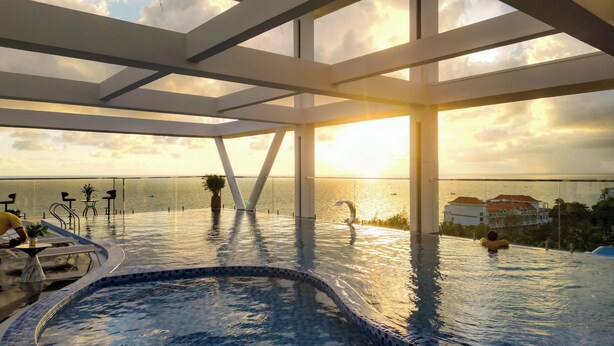 Una piscina infinita con vistas a la puesta de sol sobre el océano, rodeada por una estructura arquitectónica moderna con barandillas de cristal.