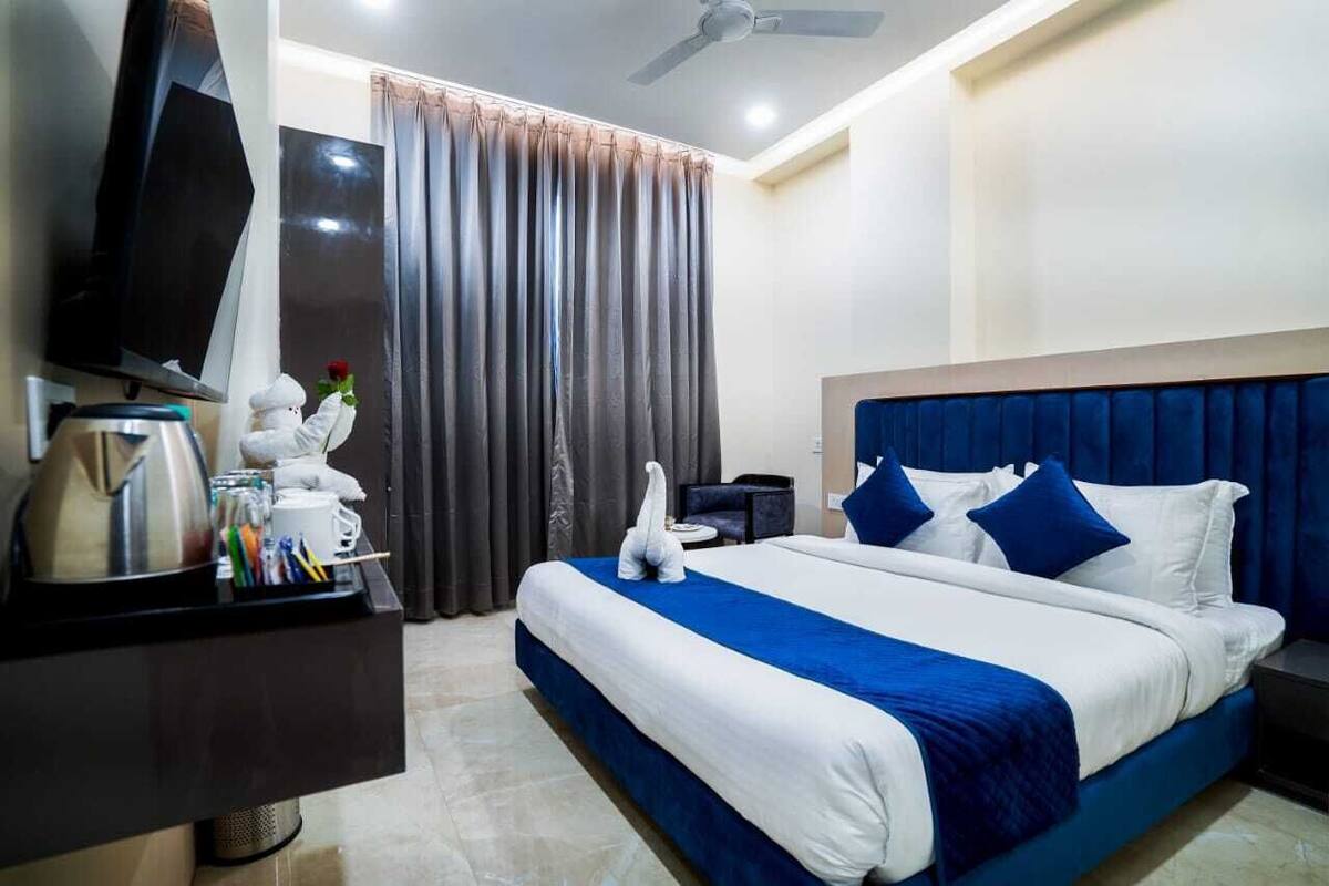 A hotel room with a bed, a TV, a desk with a kettle and pens, and a curtain.