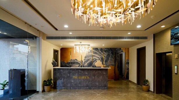 Zona de recepción con mostrador de mármol que indica "THE ELITE'S", un candelabro moderno y una gran obra de arte abstracto en la pared.