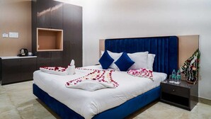Una cama bien hecha con un cabecero azul, ropa de cama blanca y pétalos de rosa decorativos.