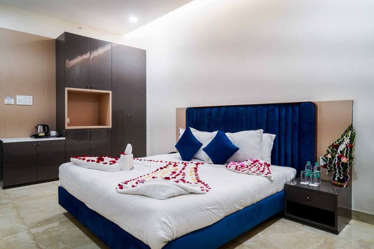A neatly made bed with a blue headboard, white bedding, and decorative rose petals.