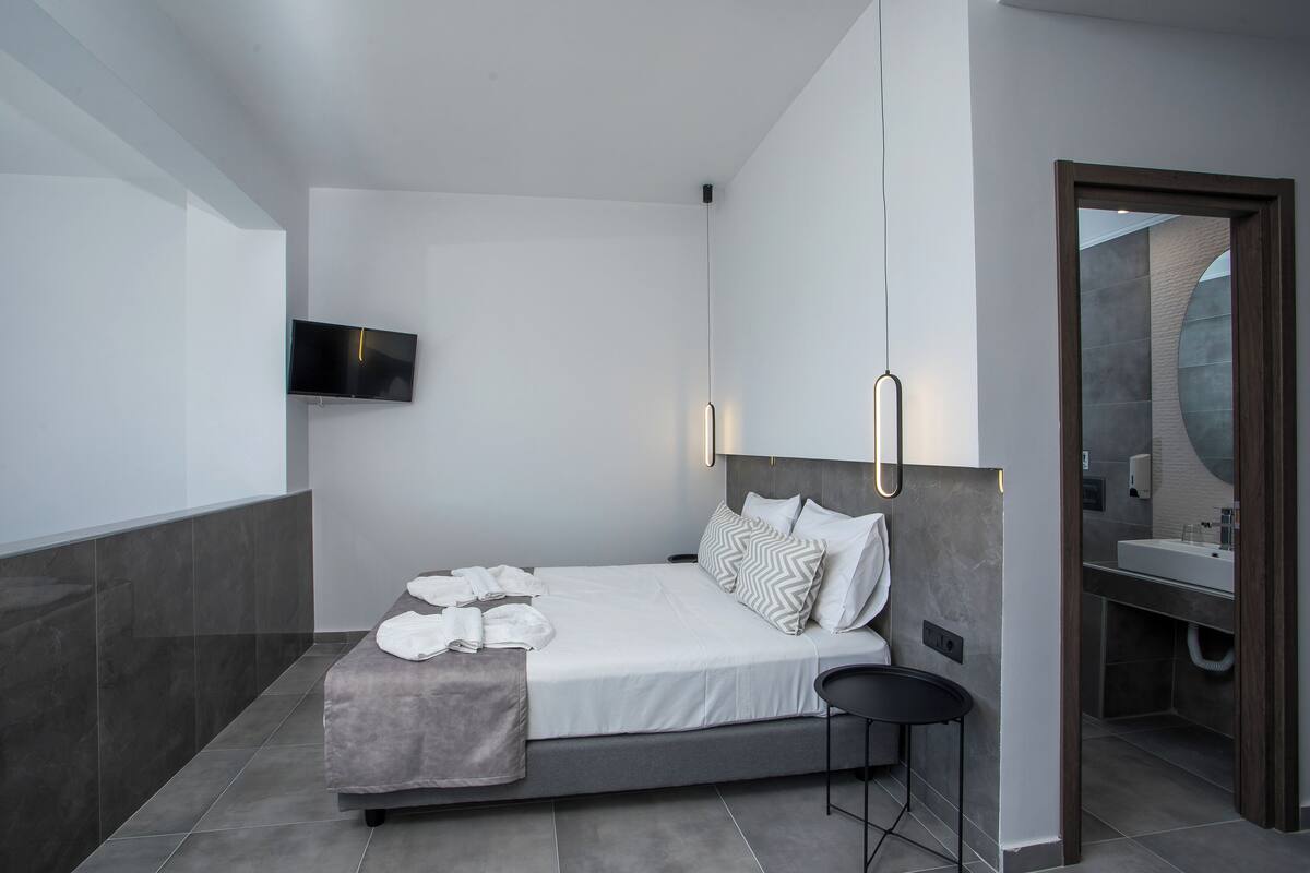 Un dormitorio moderno con cama, televisor de pantalla plana y baño con espejo y lavamanos.