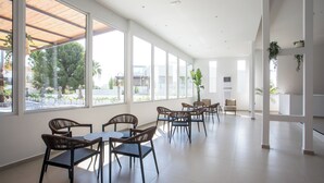 A spacious indoor area with large windows, multiple seating arrangements, and indoor plants. - Lime Hotel Faliraki (Faliraki)