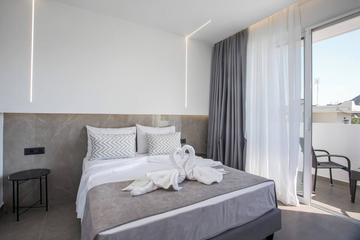Una habitación de hotel moderna con una cama grande, una mesita auxiliar pequeña y un balcón con una silla.