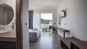 A modern hotel room with a large bed, a bathroom with a round mirror, a desk, and a TV mounted on the wall. - Lime Hotel Faliraki (Faliraki)