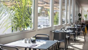A restaurant with tables and chairs, large windows, and indoor plants. - Lime Hotel Faliraki (Faliraki)
