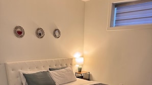 Ein Schlafzimmer mit einer gepolsterten Kopfstütze, einem Bett mit dunkelbrauner Bettdecke, weißen Kissen und einem kleinen Nachttisch mit Lampe.