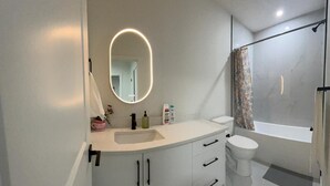 Ein modernes Badezimmer mit weißem Waschtisch, einem runden Spiegel, einer Toilette und einer Duschkabine.