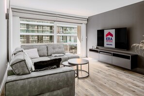 Ein modernes Wohnzimmer mit einem grauen Sofa, einem kleinen runden Tisch und einem an der Wand befestigten Flachbildfernseher.