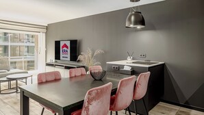 Eine moderne Küche mit Essbereich, ausgestattet mit einer großen Kochinsel, rosafarbenen Stühlen und einem Fernseher, der ein Logo für Immobilien zeigt.