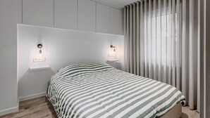 Ein modernes Schlafzimmer mit einer gestreiften Bettdecke, zwei Nachttischlampen und einem großen Fenster mit Vorhängen.
