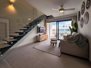 A modern living room with a glass staircase, a ceiling fan, a sofa, a TV, and a view of the outside. - 4 Bedroom Beach Penthouse w private rooftop (Punta Cana)