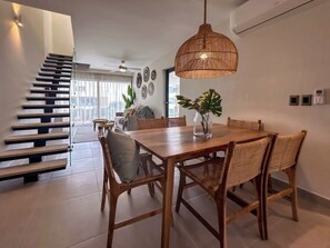 Ein moderner Essbereich mit Holztisch und Korbstühlen, einer Hängelampe sowie einer Treppe mit Glastrennwand.