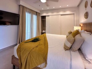 A hotel room with a large bed, a wooden headboard, a TV mounted on the wall, a wardrobe, and a window with curtains. - 4 Bedroom Beach Penthouse w private rooftop (Punta Cana)