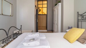 A hotel room with a neatly made bed, a yellow pillow, and a bathroom visible through an open door.