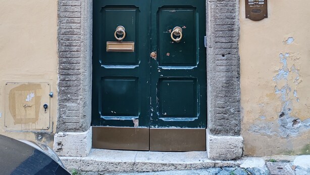 A green double door with a metal handle and a nameplate, set in a stone archway above a beige wall with the number 19.