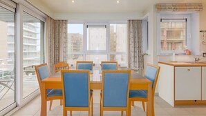 A modern apartment with a dining area, kitchen, and large windows offering views of the city. - Apollo II 0203 met garage (NIEUWPOORT)