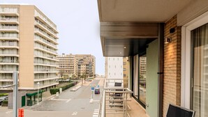 A balcony with a view of a city street, a building with a green facade, and a parked car. - Apollo II 0203 met garage (NIEUWPOORT)
