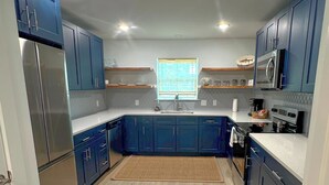 A modern kitchen with dark blue cabinets, stainless steel appliances, and a wooden floor.